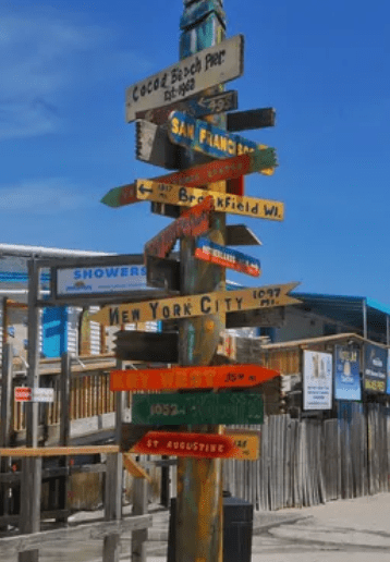 A signpost at Cocoa Beach Pier with signs pointing to different cities.