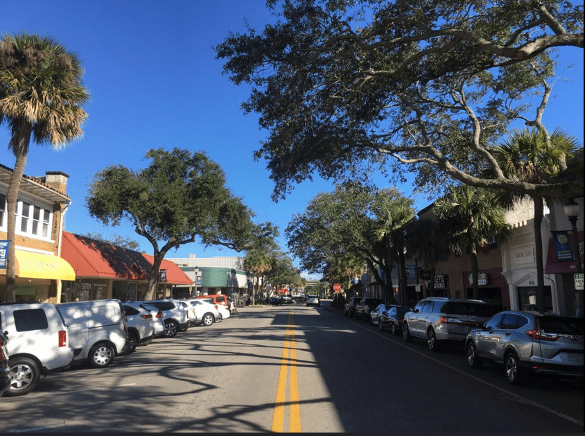A daytime street view of Strawbridge Avenue in downtown Melbourne, Florida, showing cars parked on both sides of a two-lane road lined with businesses and palm trees.