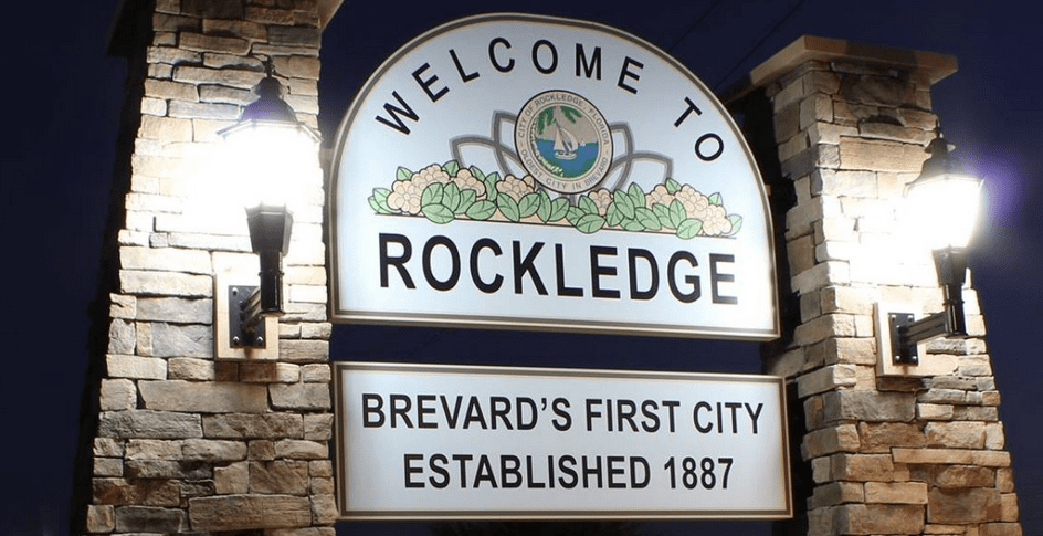 A "Welcome to Rockledge, Brevard's First City" sign lit up at night.