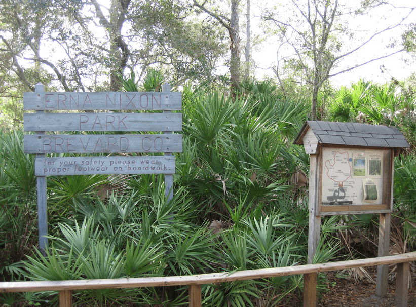The wooden entrance sign for Erna Nixon Park in West Melbourne, Florida, surrounded by lush vegetation.